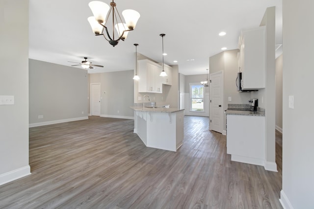 kitchen with ceiling fan with notable chandelier, light hardwood / wood-style floors, white cabinets, decorative light fixtures, and kitchen peninsula