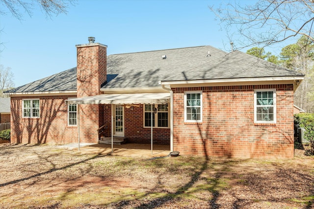 rear view of house with entry steps, a shingled roof, brick siding, a chimney, and a patio area