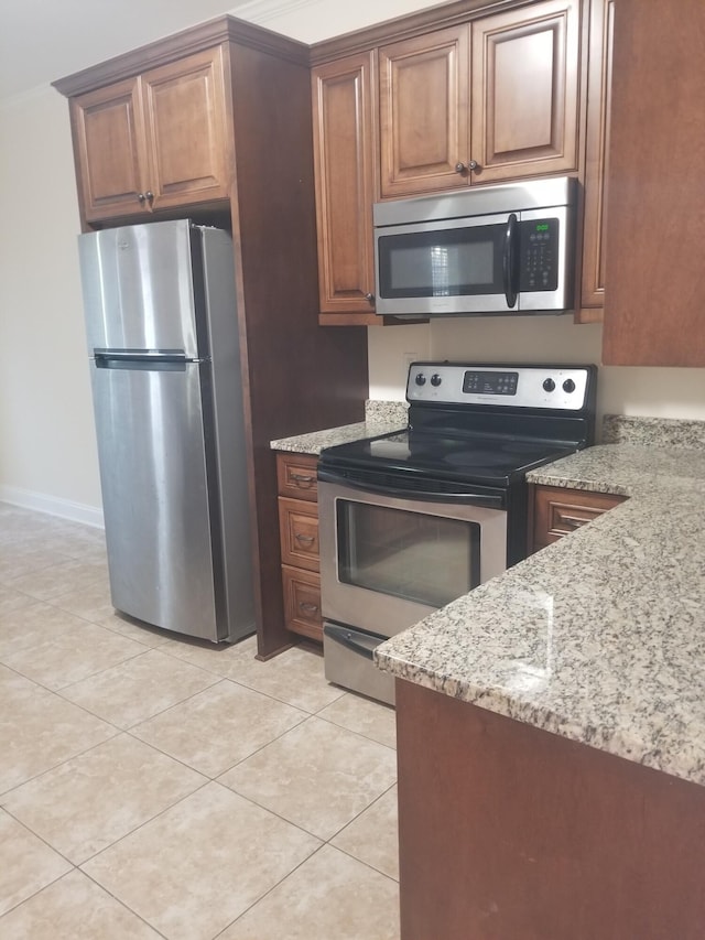 kitchen with light tile patterned floors, light stone countertops, baseboards, appliances with stainless steel finishes, and brown cabinets