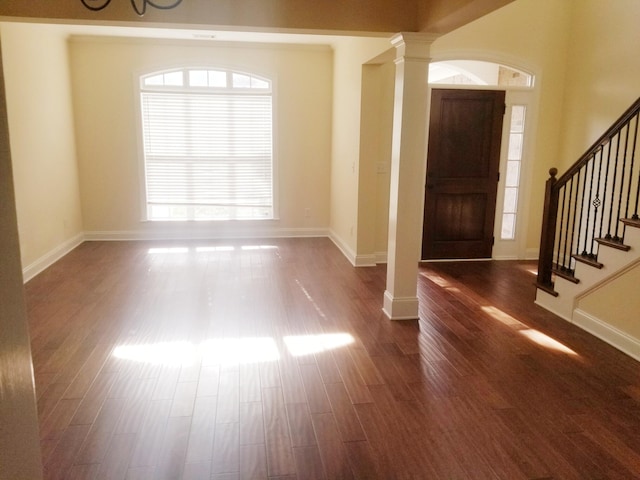 foyer entrance featuring dark wood-style floors, plenty of natural light, stairway, and ornate columns