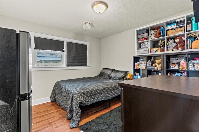 bedroom featuring baseboards, a textured ceiling, wood finished floors, and freestanding refrigerator