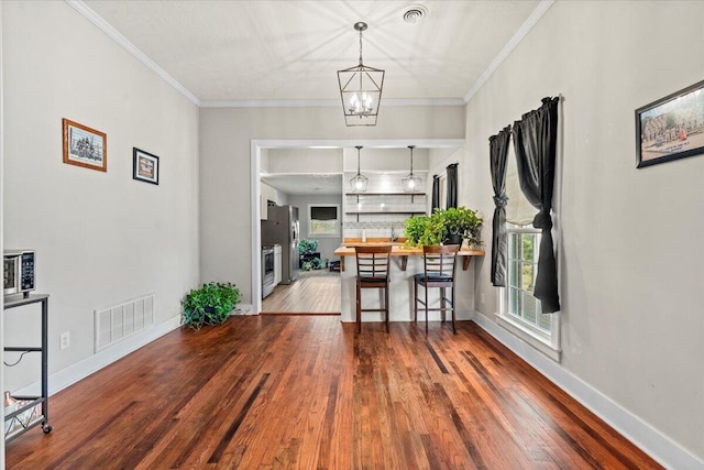 dining space featuring visible vents, baseboards, wood finished floors, and crown molding