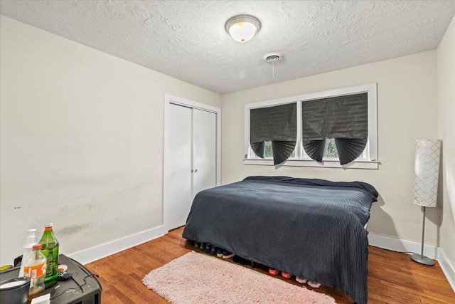 bedroom with wood finished floors, visible vents, baseboards, a closet, and a textured ceiling