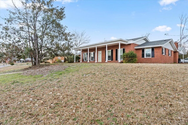 view of front of home with brick siding, a porch, a chimney, and a front yard