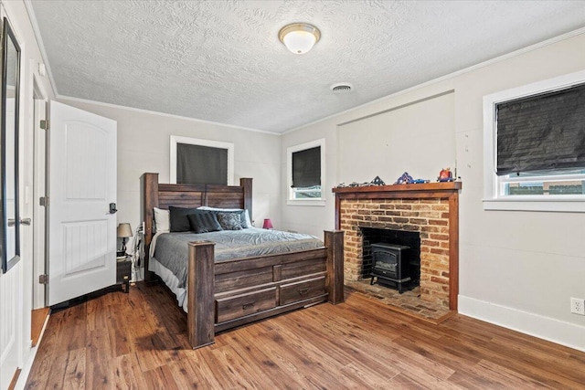 bedroom with visible vents, ornamental molding, a wood stove, and wood finished floors