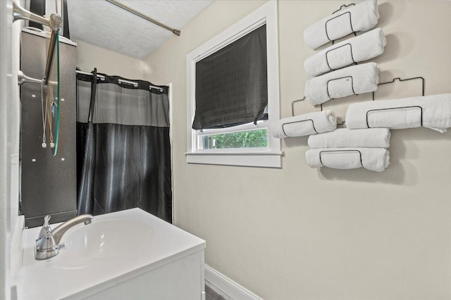 bathroom featuring curtained shower, a sink, baseboards, and a textured ceiling