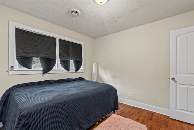 bedroom featuring a textured ceiling, wood finished floors, visible vents, and baseboards