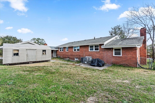 back of property with an outbuilding, fence, a yard, brick siding, and a chimney