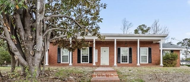 view of front facade with brick siding, covered porch, and a front lawn