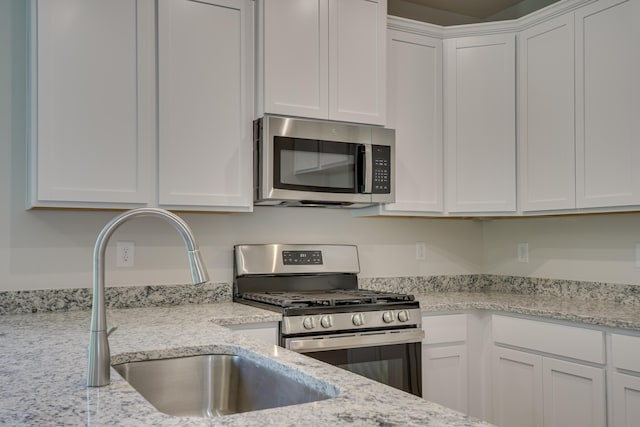 kitchen with a sink, white cabinets, appliances with stainless steel finishes, and light stone countertops