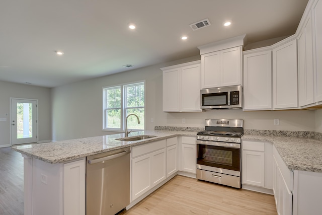kitchen featuring visible vents, a peninsula, a sink, light wood-style floors, and appliances with stainless steel finishes