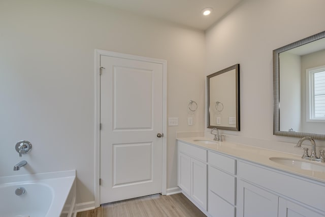 bathroom with a sink, wood finished floors, a bath, and double vanity