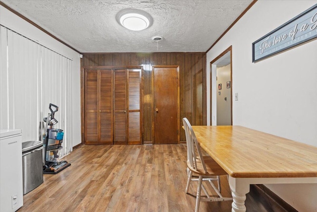 dining room featuring wood walls, light wood-type flooring, ornamental molding, and a textured ceiling