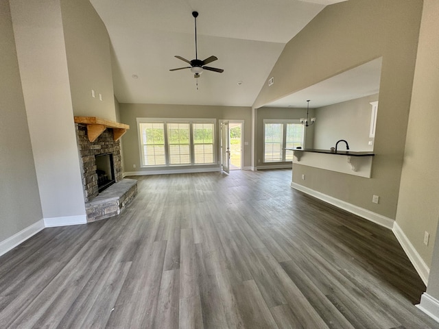 unfurnished living room with baseboards, dark wood-style flooring, ceiling fan with notable chandelier, high vaulted ceiling, and a fireplace