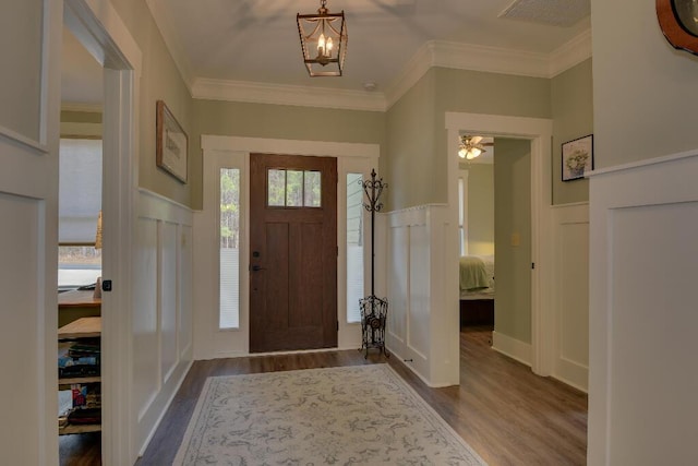 foyer entrance featuring wood-type flooring, ornamental molding, and a notable chandelier