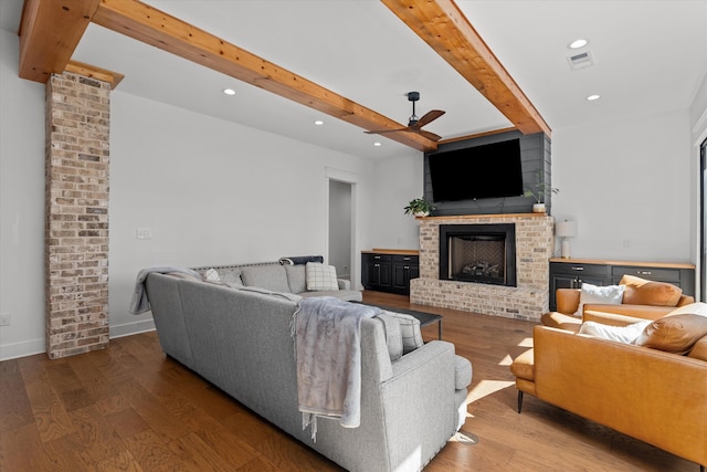 living area with beam ceiling, a brick fireplace, wood finished floors, and ceiling fan