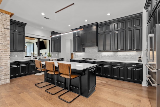 kitchen with visible vents, light countertops, light wood-style floors, dark cabinets, and a center island