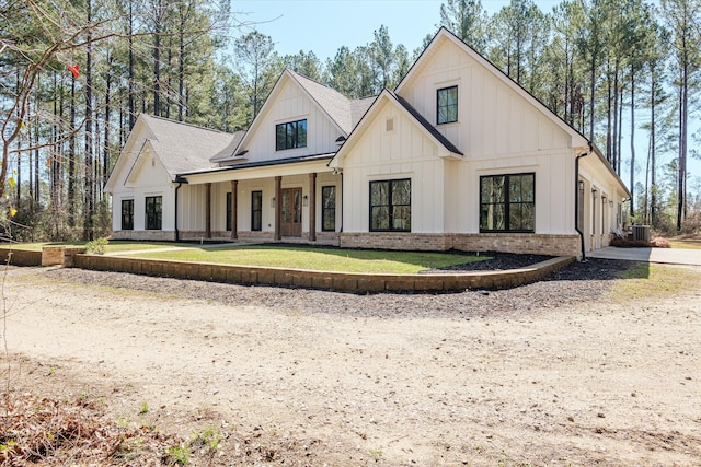 modern farmhouse with covered porch, board and batten siding, a shingled roof, and a front lawn