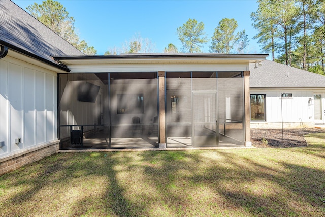 rear view of property with a yard, board and batten siding, a sunroom, and a shingled roof