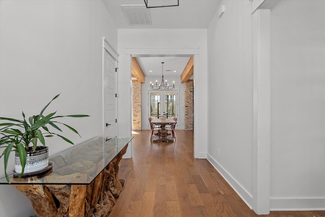 hallway featuring visible vents, wood finished floors, brick wall, baseboards, and a chandelier