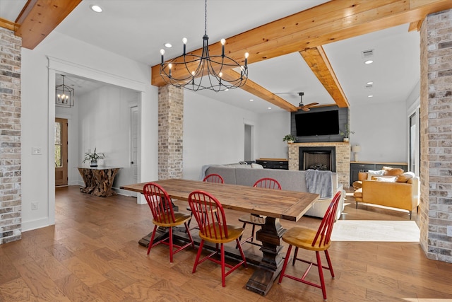 dining room with a brick fireplace, beamed ceiling, recessed lighting, ceiling fan with notable chandelier, and wood finished floors