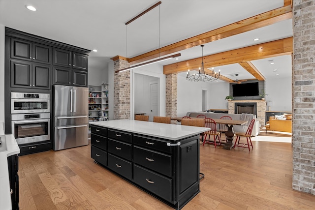 kitchen featuring appliances with stainless steel finishes, a center island, dark cabinetry, and light wood-style floors