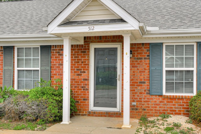 doorway to property featuring brick siding and a shingled roof