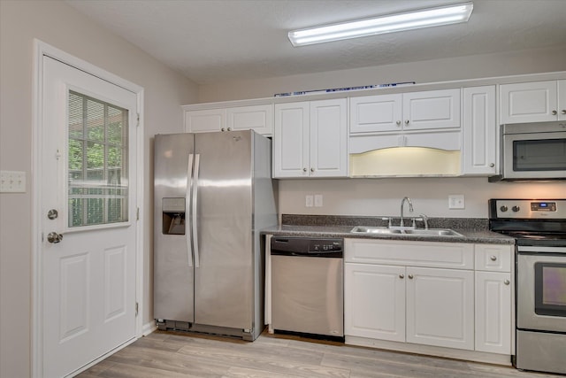 kitchen with dark countertops, a sink, white cabinets, stainless steel appliances, and light wood-style flooring