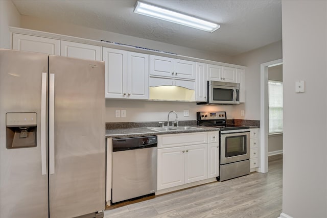 kitchen featuring dark countertops, a sink, white cabinets, stainless steel appliances, and light wood-style flooring