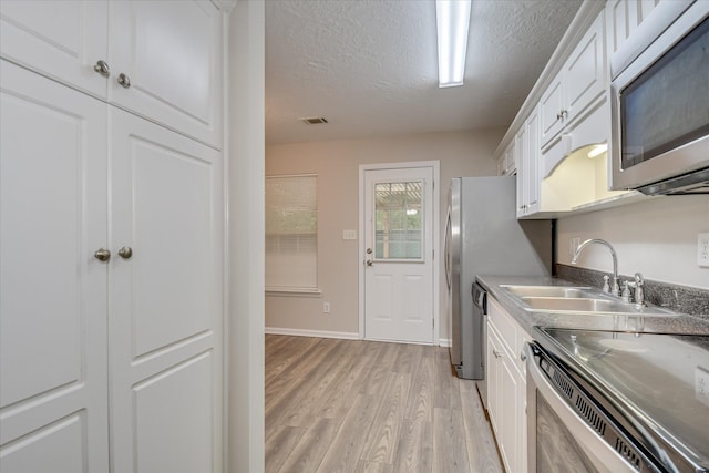 kitchen with a textured ceiling, appliances with stainless steel finishes, a sink, white cabinets, and light wood-style flooring