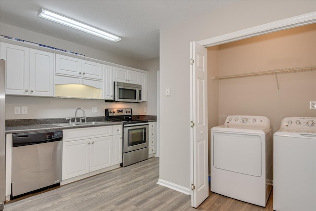 kitchen with dark countertops, washing machine and dryer, a sink, stainless steel appliances, and light wood-style flooring