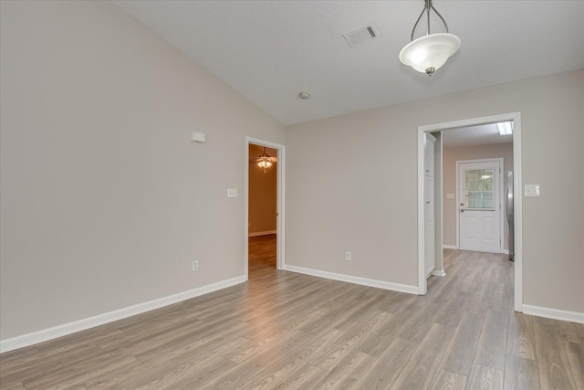 unfurnished room with visible vents, light wood-style flooring, baseboards, and vaulted ceiling