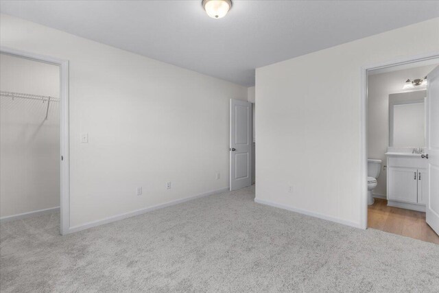 unfurnished bedroom with ensuite bath, a walk in closet, a closet, and light colored carpet