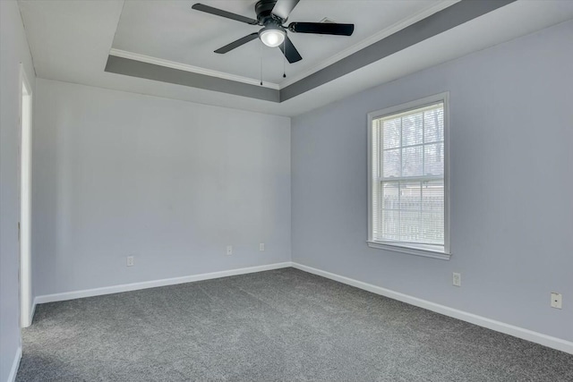 unfurnished room featuring a tray ceiling, dark carpet, and baseboards