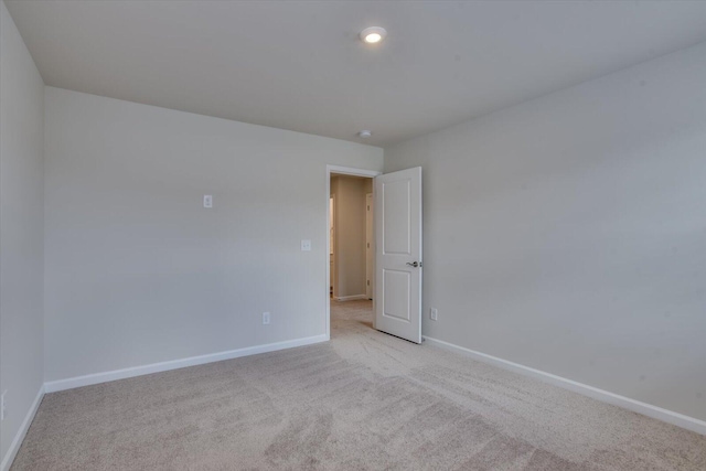 spare room with baseboards, recessed lighting, and light colored carpet