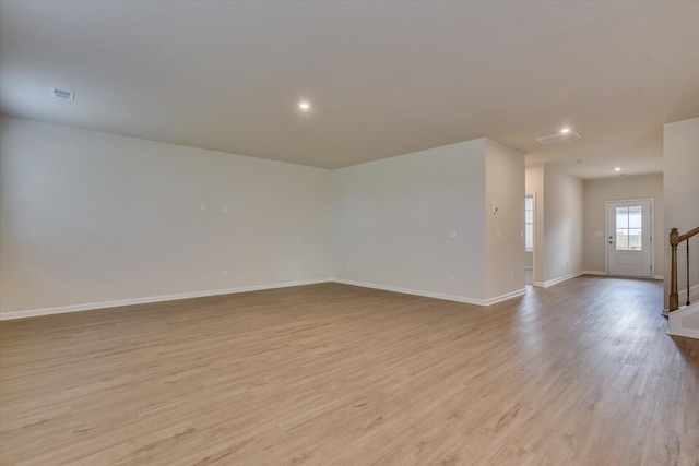 empty room with visible vents, light wood-style flooring, baseboards, and stairs