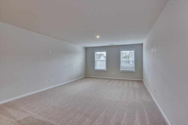 spare room featuring light colored carpet and baseboards