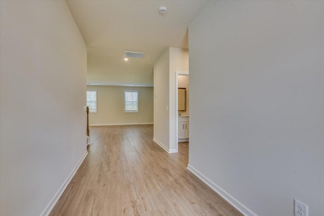 hallway featuring baseboards, visible vents, and light wood finished floors