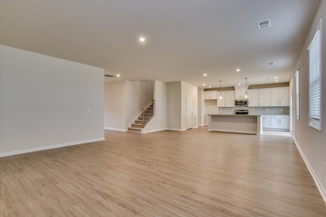 unfurnished living room featuring stairs, light wood-style flooring, visible vents, and baseboards