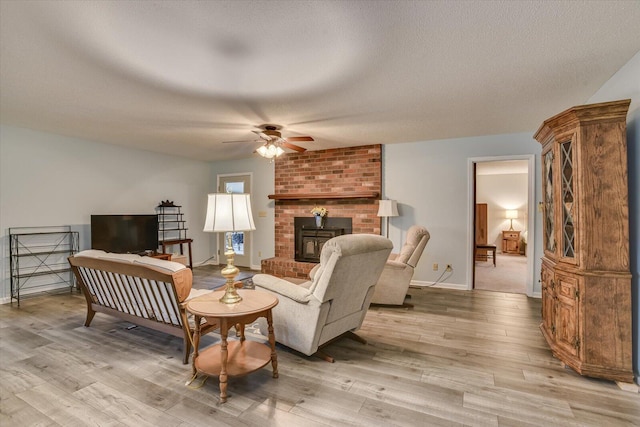 living room with a wood stove, ceiling fan, light hardwood / wood-style flooring, and a textured ceiling