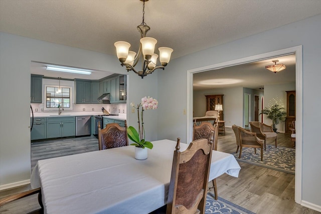 dining area with a textured ceiling, light wood-type flooring, sink, and a chandelier