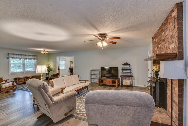 living room with a textured ceiling, ceiling fan, light wood-type flooring, and a fireplace