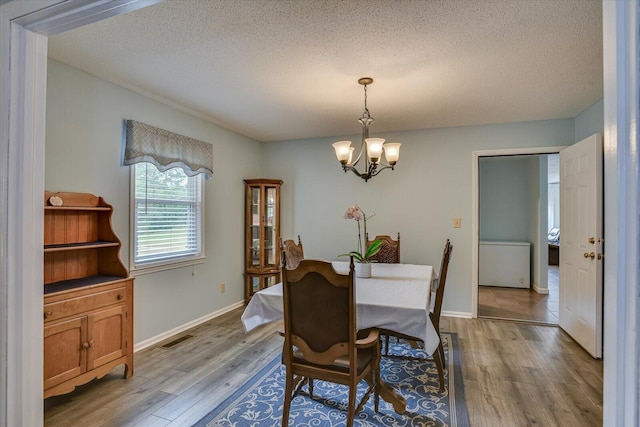 dining space with a textured ceiling, light hardwood / wood-style floors, and a notable chandelier