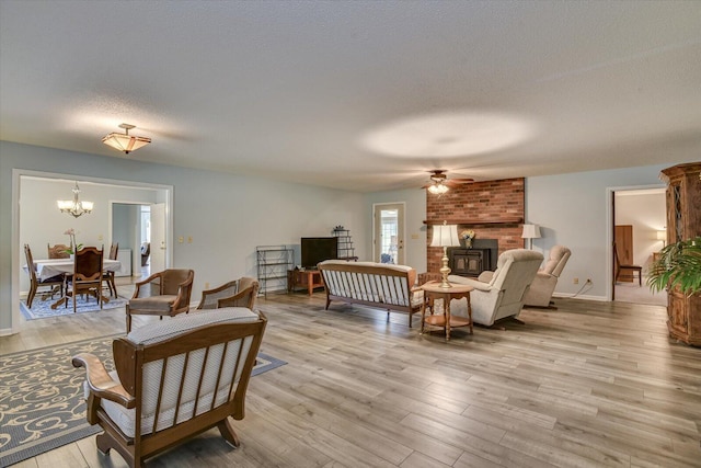 living room featuring ceiling fan with notable chandelier, a wood stove, a textured ceiling, and light hardwood / wood-style flooring