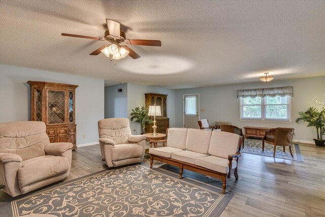 living room with ceiling fan, light hardwood / wood-style flooring, and a textured ceiling