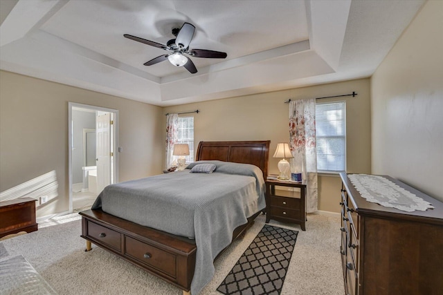 carpeted bedroom featuring a raised ceiling, ceiling fan, multiple windows, and ensuite bath