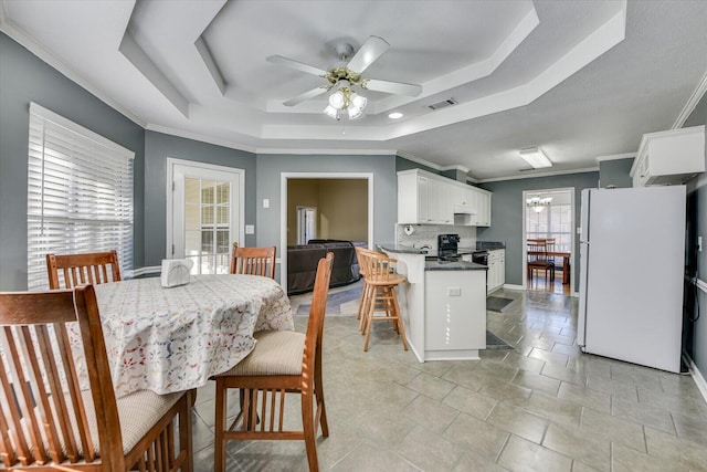 dining room with a raised ceiling, crown molding, and ceiling fan with notable chandelier