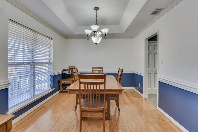 dining room featuring an inviting chandelier, ornamental molding, a raised ceiling, and light hardwood / wood-style floors