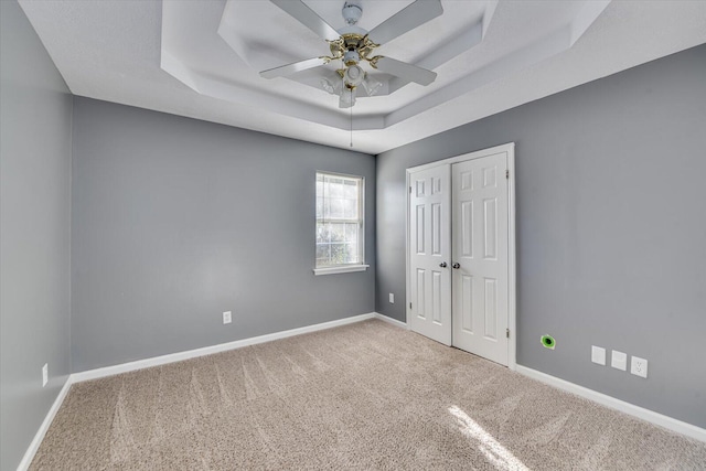 carpeted empty room featuring a raised ceiling and ceiling fan