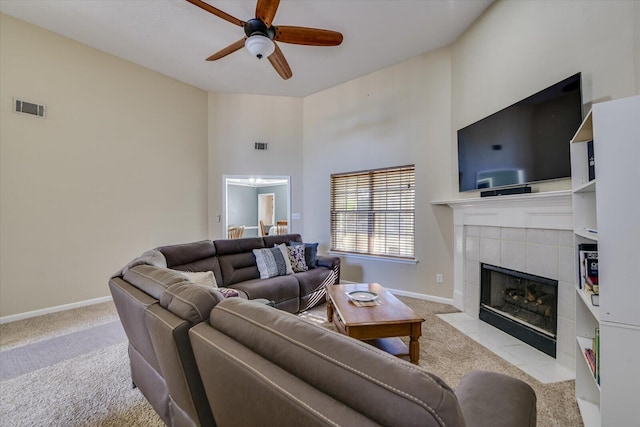 living room with a tiled fireplace, a towering ceiling, light carpet, and ceiling fan